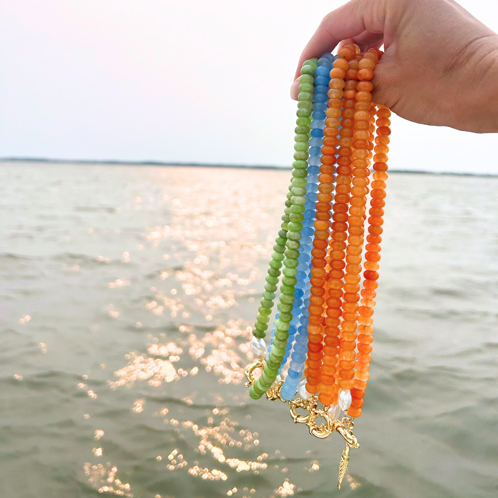 Beaded necklaces in orange, green, and blue on the water