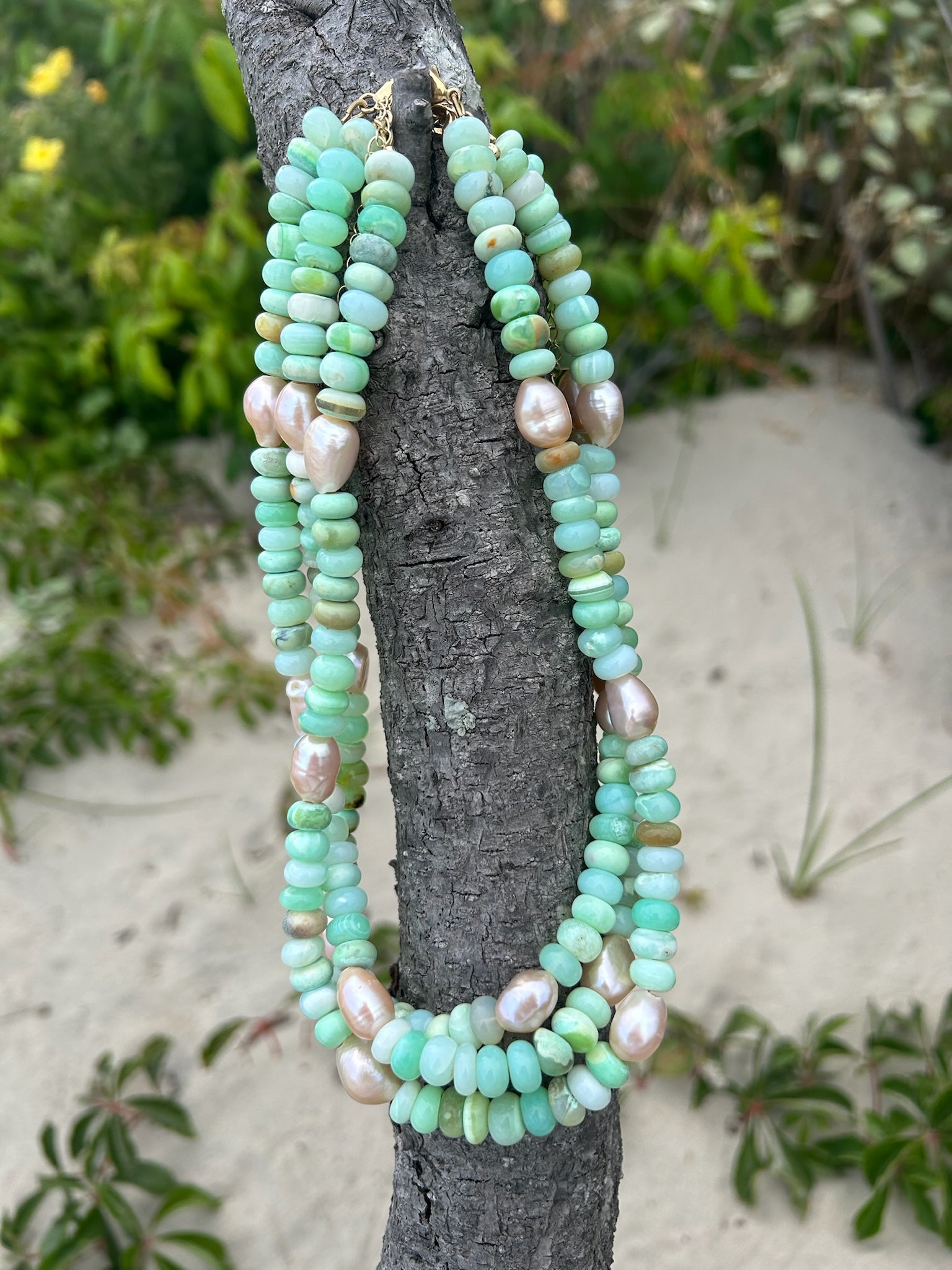 Stack of green and pink beaded necklaces on a tree branch at the beach